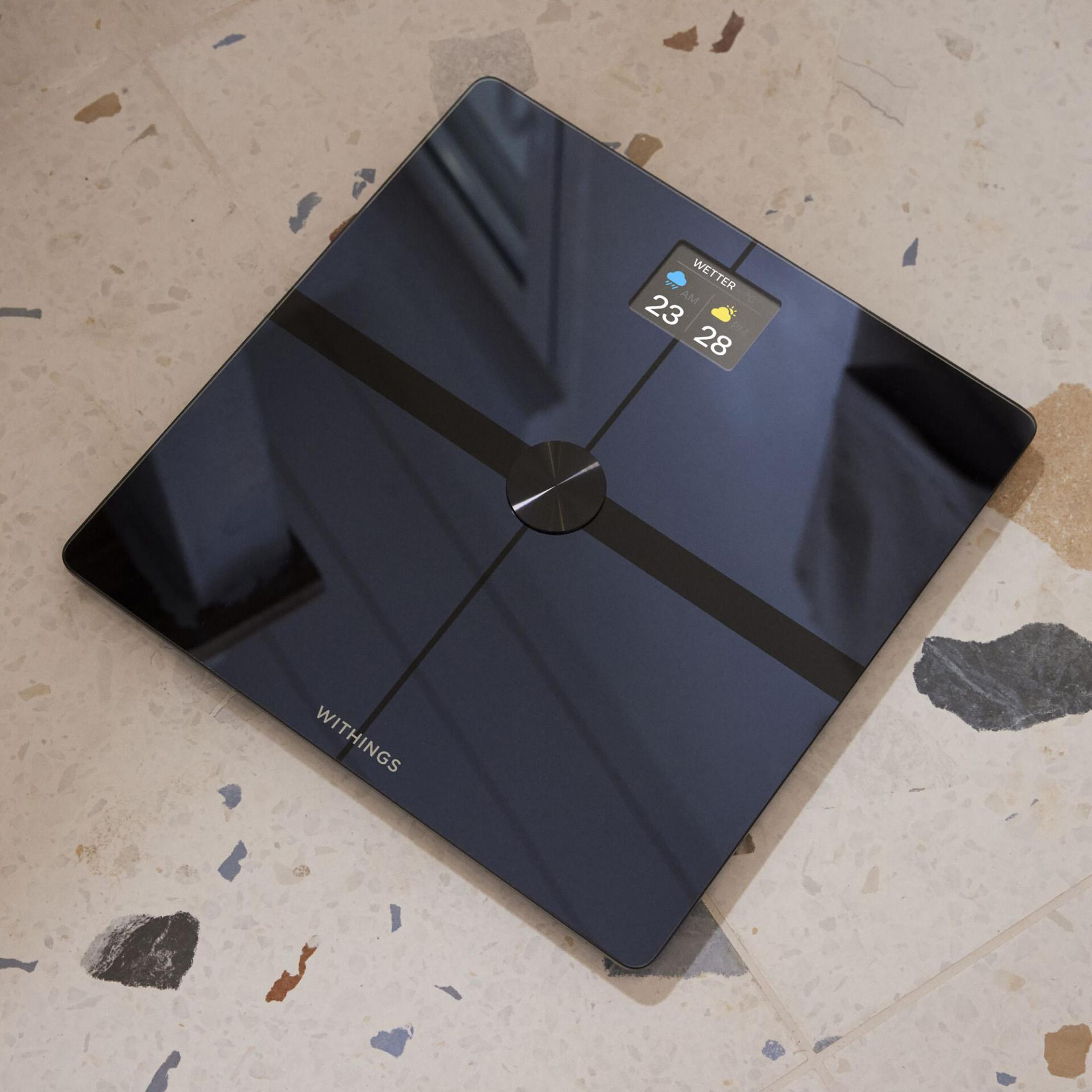 Czarna, kwadratowa inteligentna waga z wyświetlaczem pokazującym pogodę i liczby.