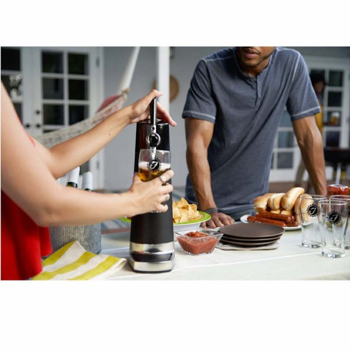 Femme versant de la bière d'un robinet dans un verre. Homme debout près d'une table avec de la nourriture.