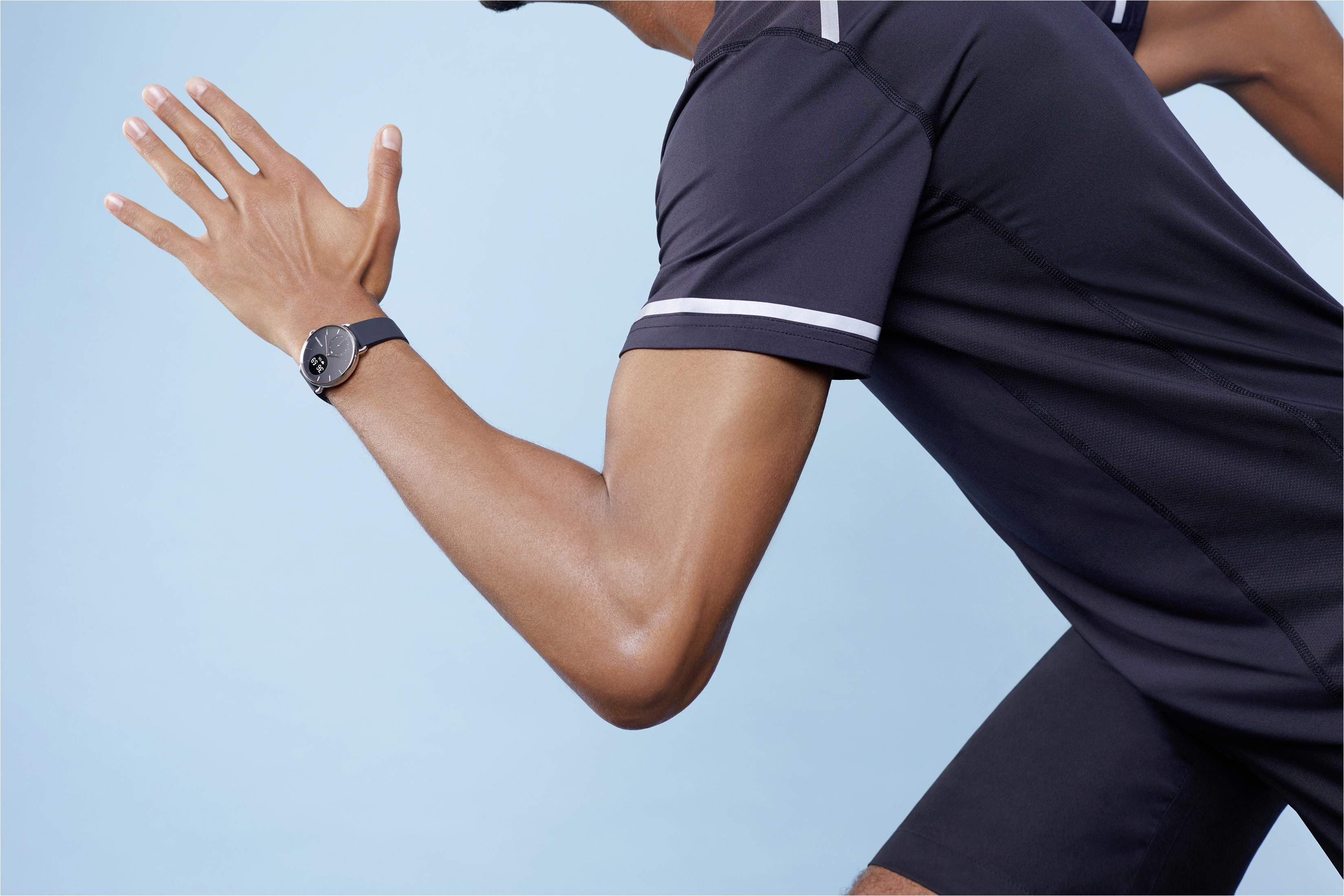 Ein Mann rennt und trägt eine Uhr am Handgelenk. Er trägt ein schwarzes Hemd und Shorts, blauer Hintergrund.