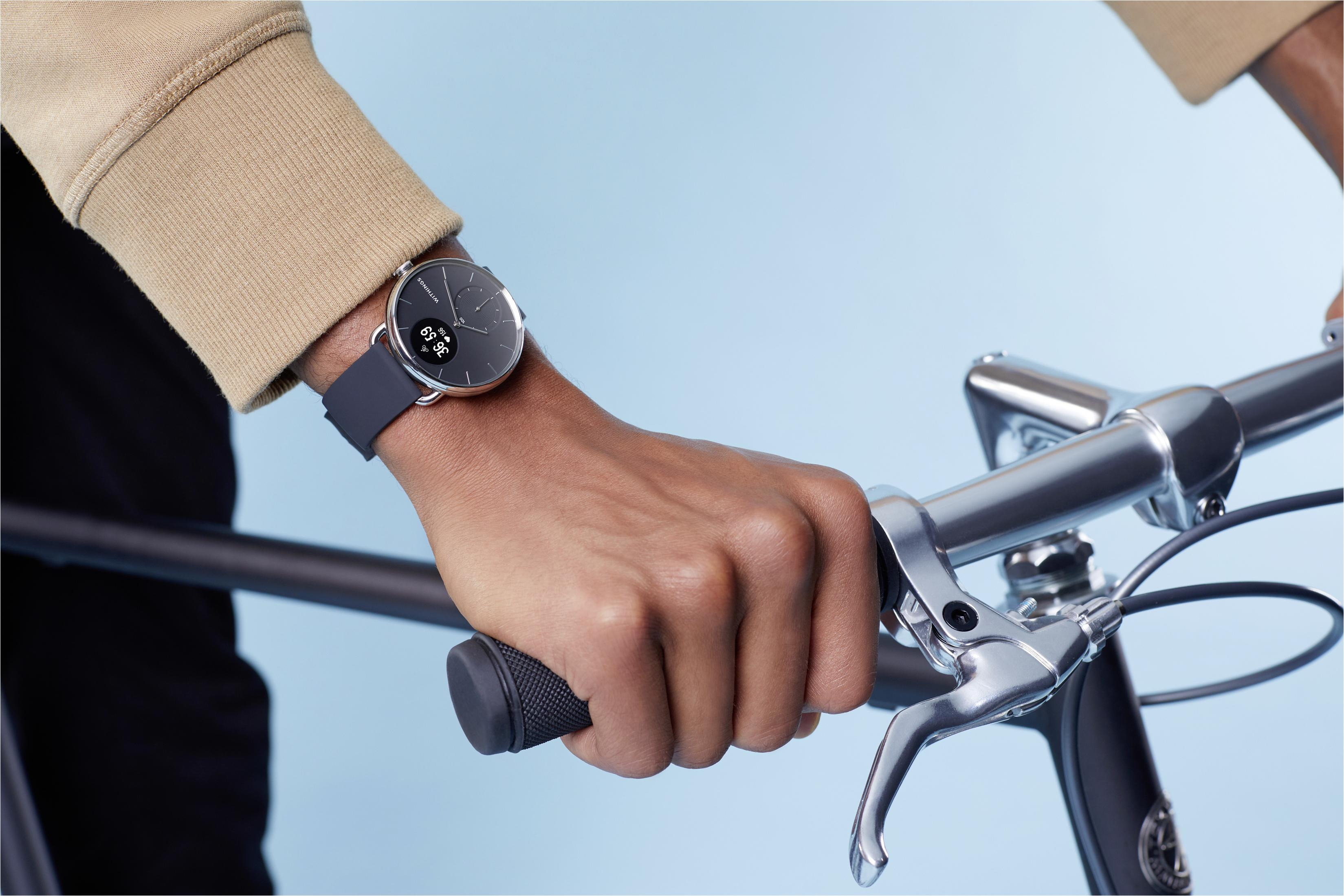 Arm einer Person mit Smartwatch an einem Fahrradlenker. Beiges Hemd, blauer Hintergrund.