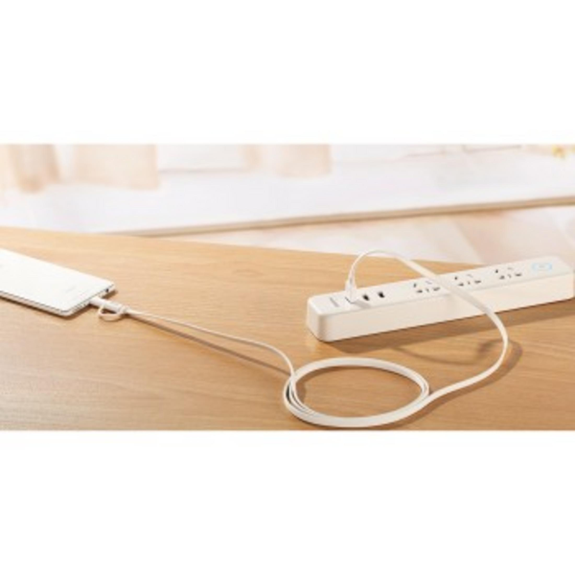 Een witte stekkerdoos met twee USB-poorten is aangesloten op een telefoon. Op een houten tafel.