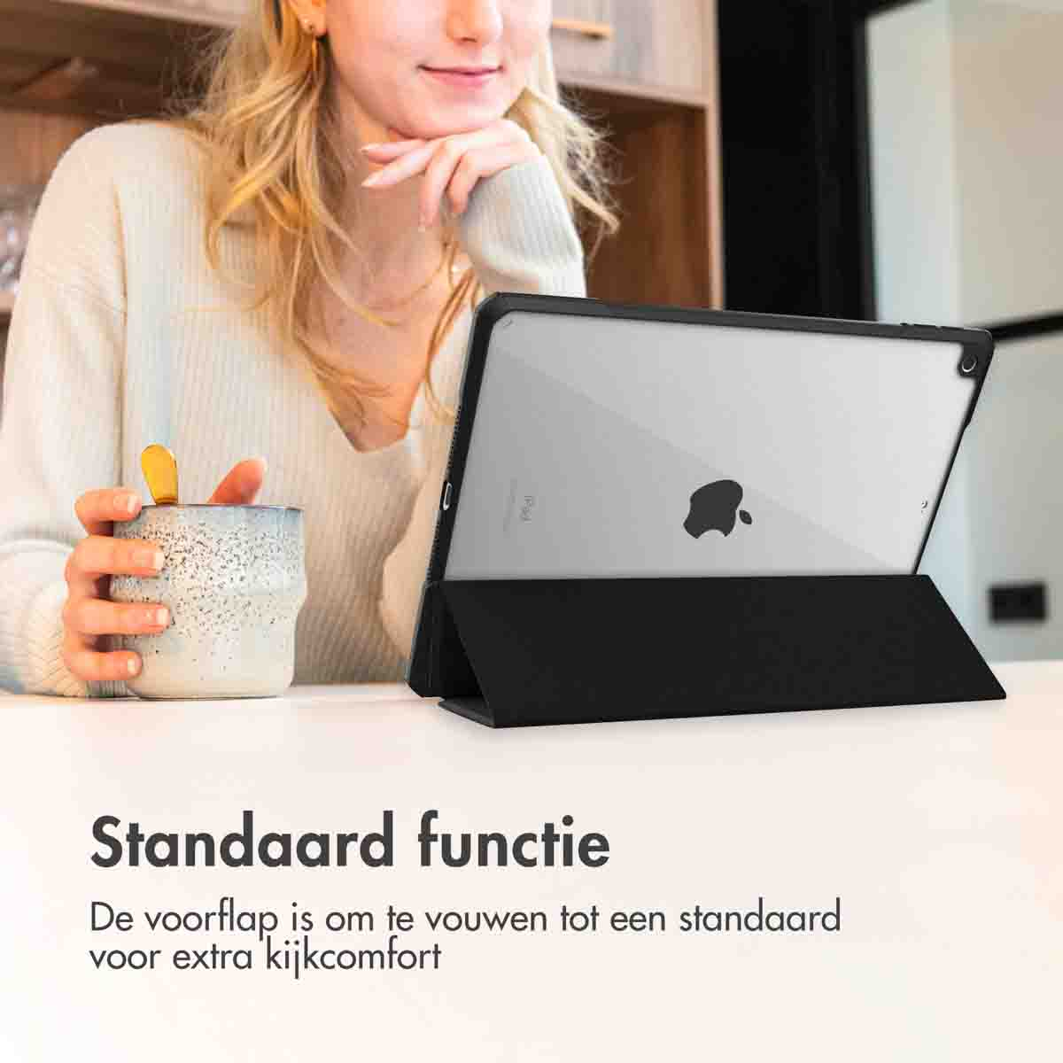 Femme aux cheveux blonds utilisant une tablette noire avec un support. Une tasse est sur la table.