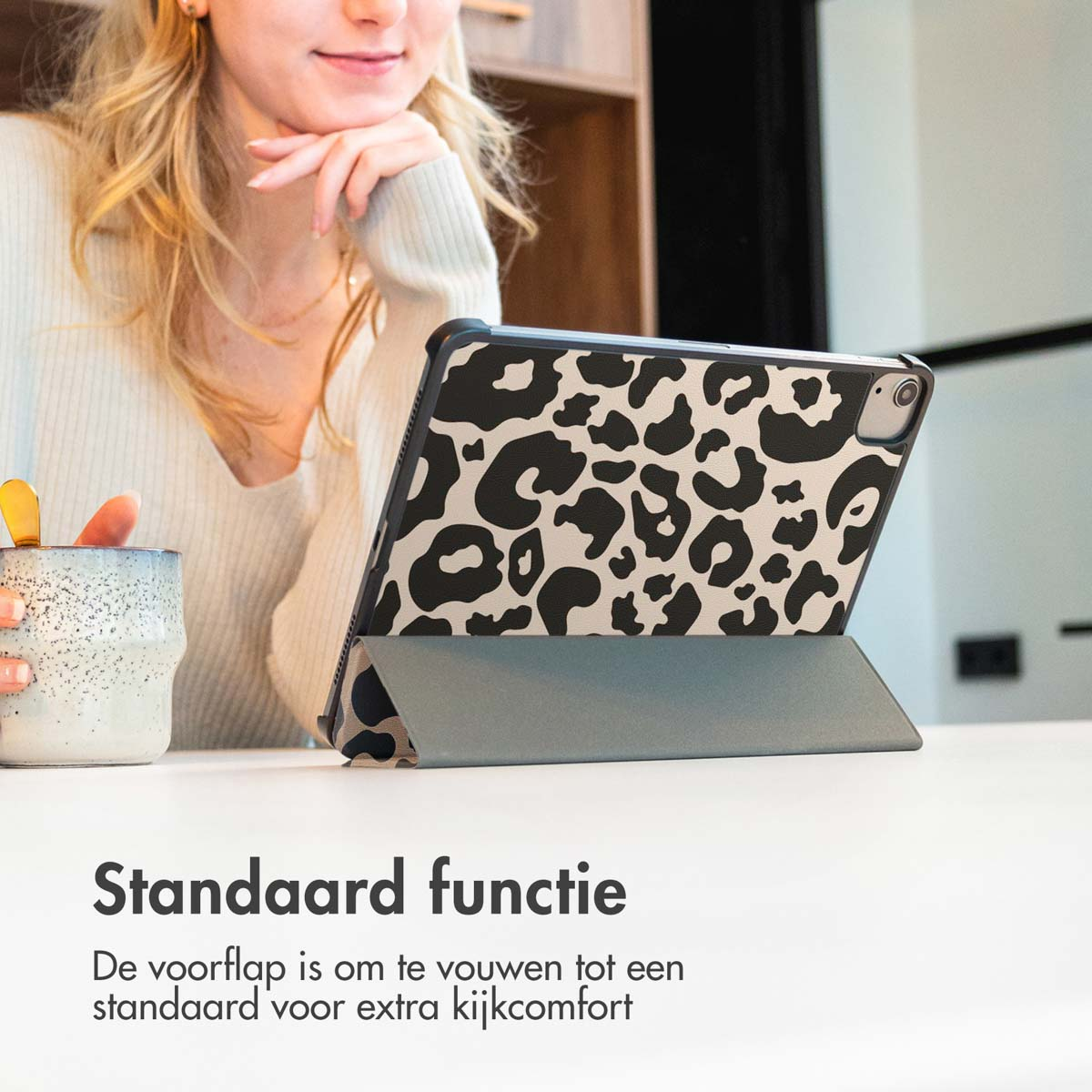 Vrouw met een tablet in een hoes met een luipaardprint. Zittend aan een tafel.