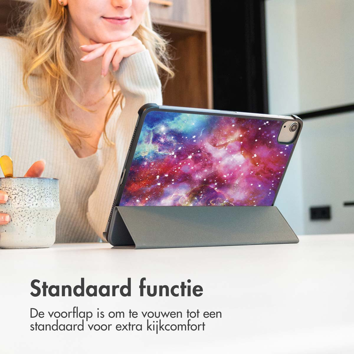 Une femme avec une tasse blanche, regardant un iPad dans un étui. L'écran affiche un motif de galaxie.