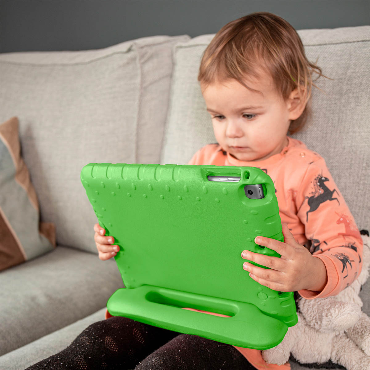 Een kind dat op een bank zit, houdt een groene tablet met een groene hoes vast.