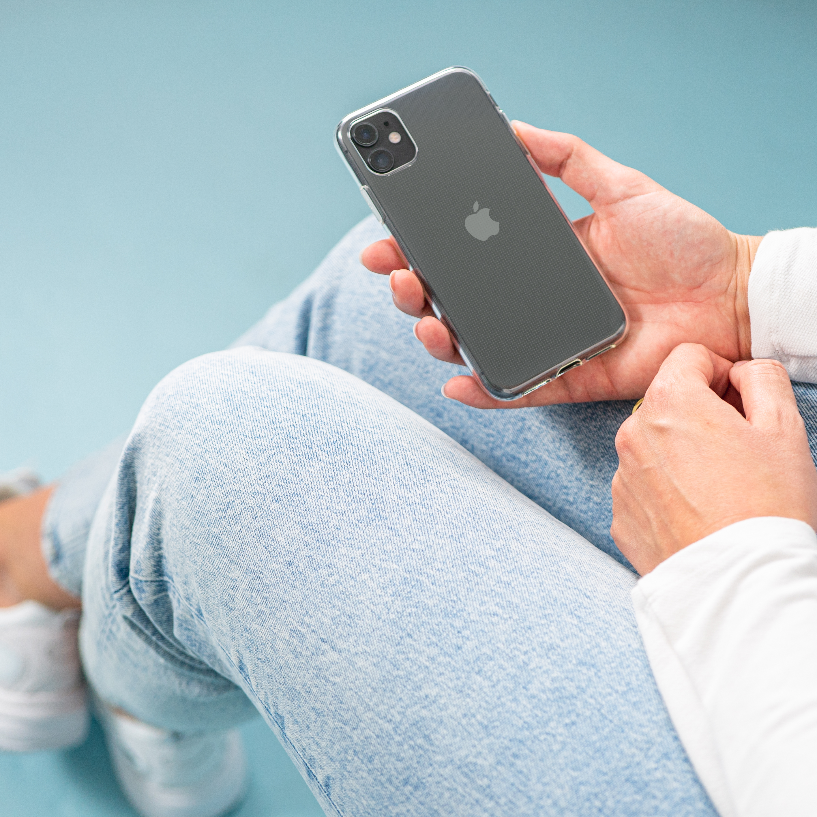 A person holding a black phone with a clear case. They are wearing blue jeans.