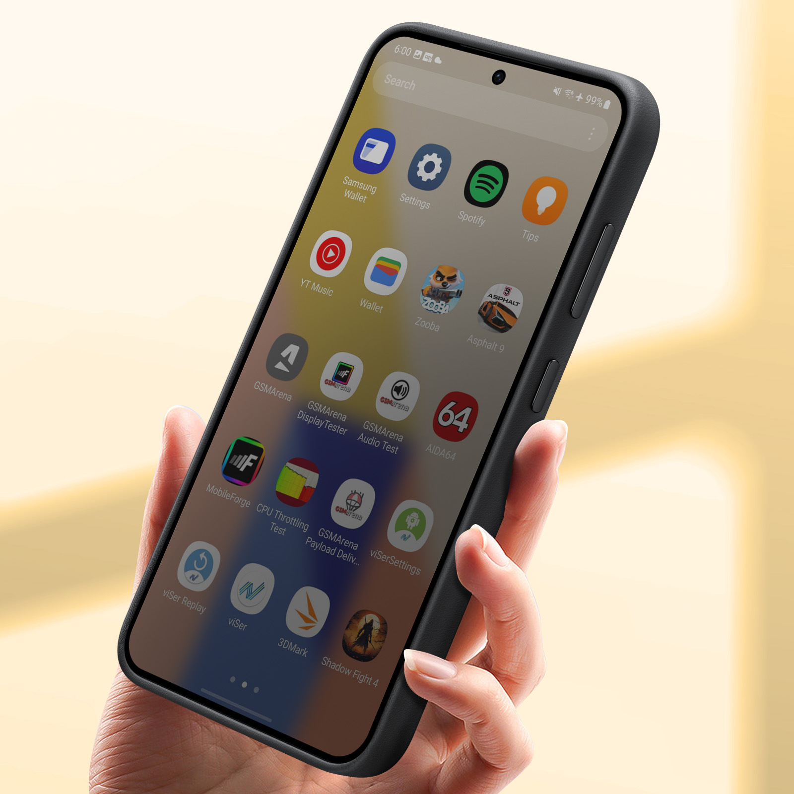 Dłoń trzymająca czarny telefon, wyświetlająca ikony aplikacji. Złote tło.