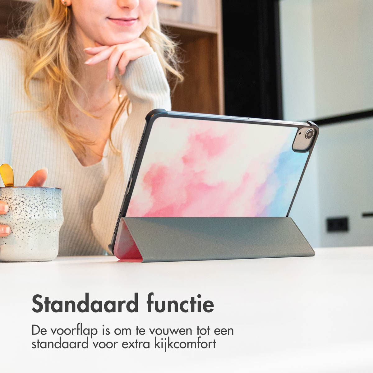 Een vrouw bekijkt een tablet in een hoesje. De hoes is opgezet als standaard. De achtergrond is een keuken.
