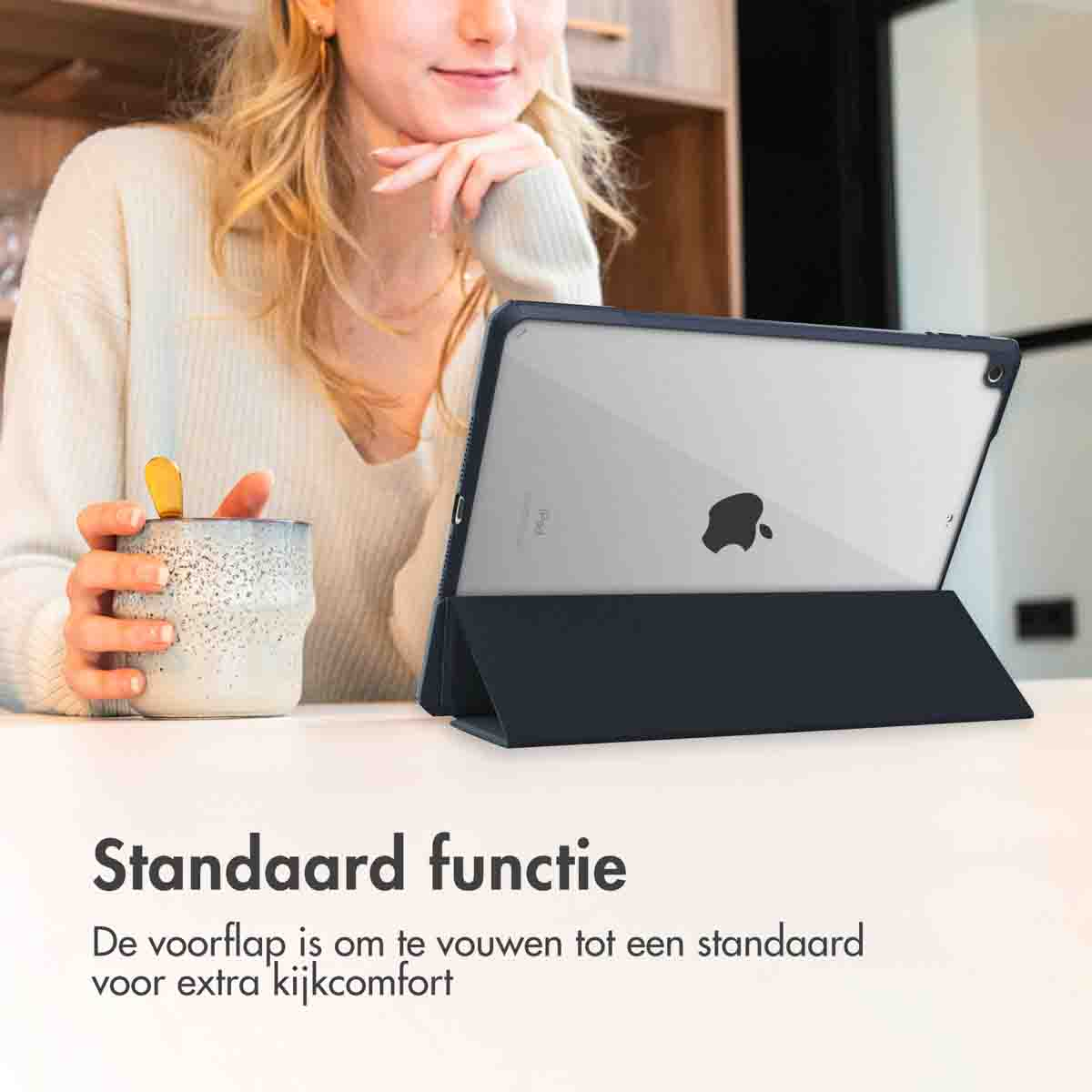 Une femme assise à une table avec une tablette dans un étui bleu foncé et une tasse de café.