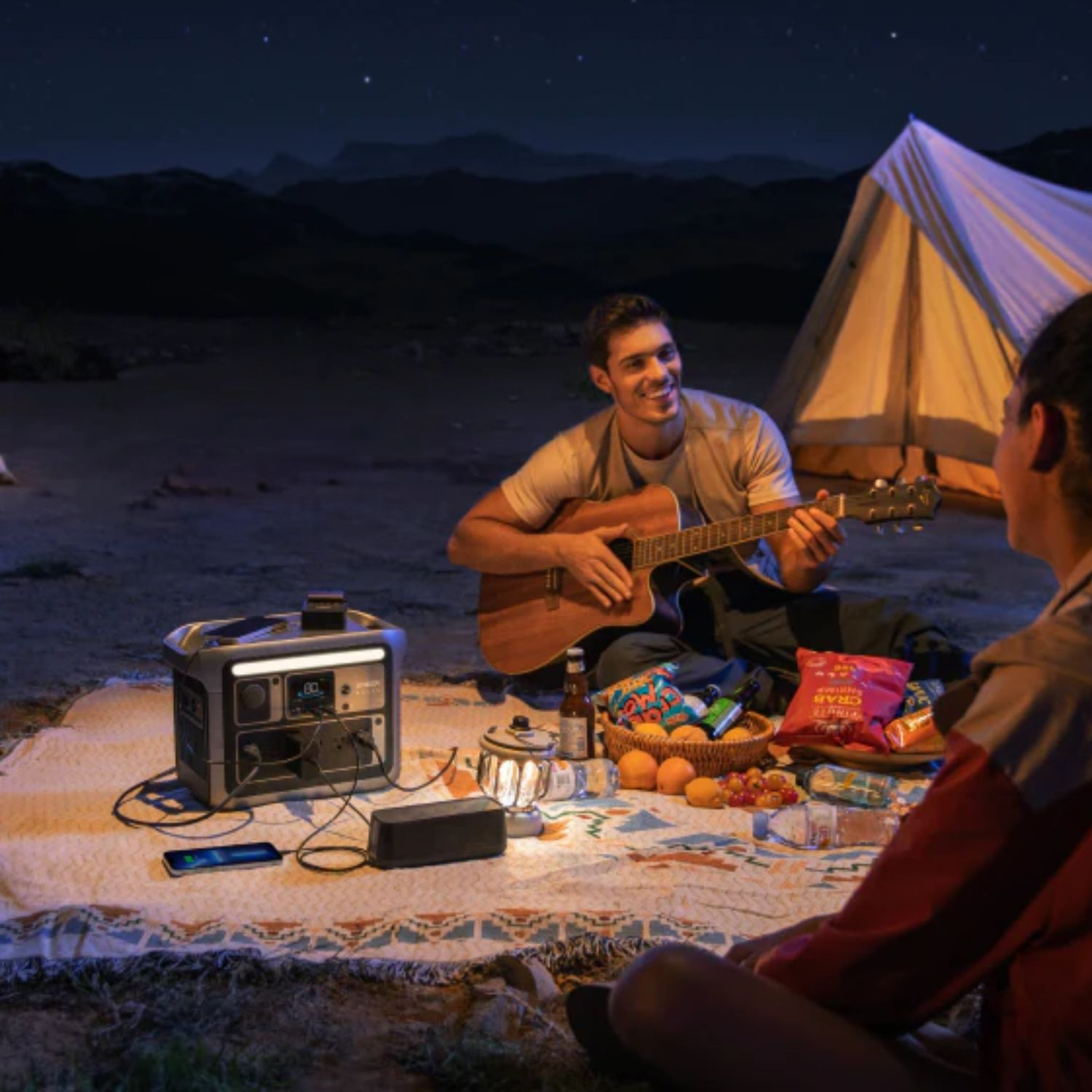 Ludzie biwakują, grają na gitarze, jedzenie i elektrownia pod gwiaździstym niebem.