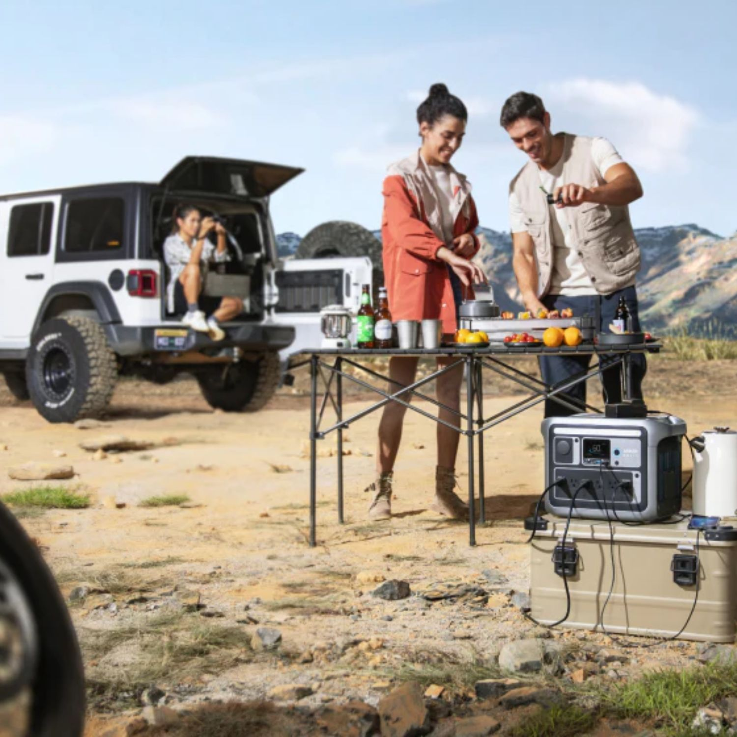 Ludzie gotują na zewnątrz w pobliżu białego SUV-a. Jest stół z jedzeniem i stacja zasilania.