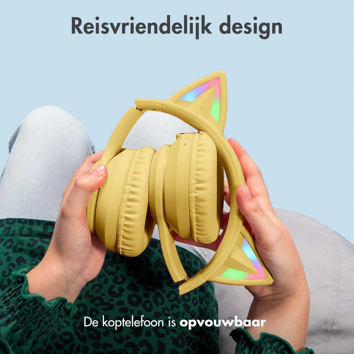 Handen houden gele koptelefoon met kattenoren vast. De koptelefoon is opgevouwen. Blauwe achtergrond.