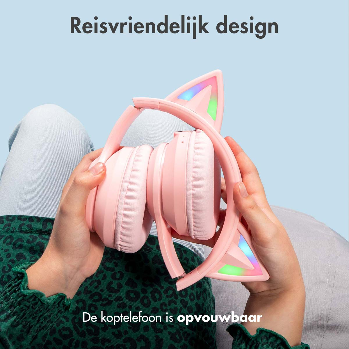 Hands holding pink cat ear headphones. The headphones are folded. Light blue background.