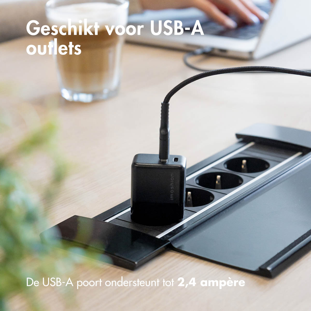 Un chargeur USB noir branché sur une multiprise. Un ordinateur portable et une tasse de café en arrière-plan.