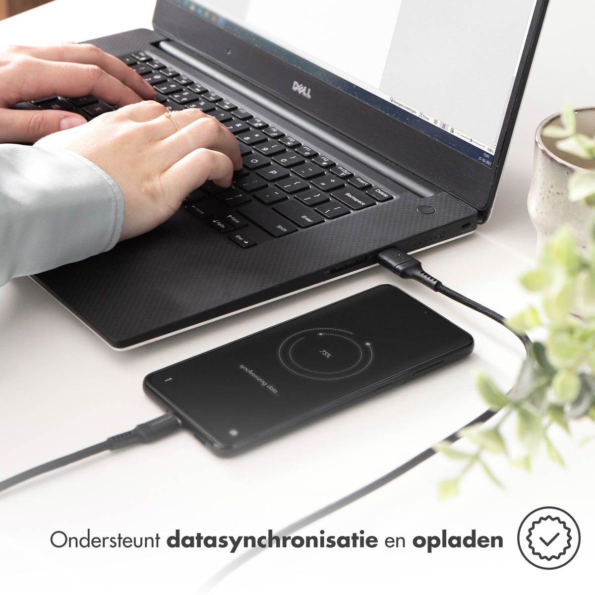 Une personne utilise un ordinateur portable avec un téléphone en charge. Le téléphone affiche 75% et est connecté à l'ordinateur portable.