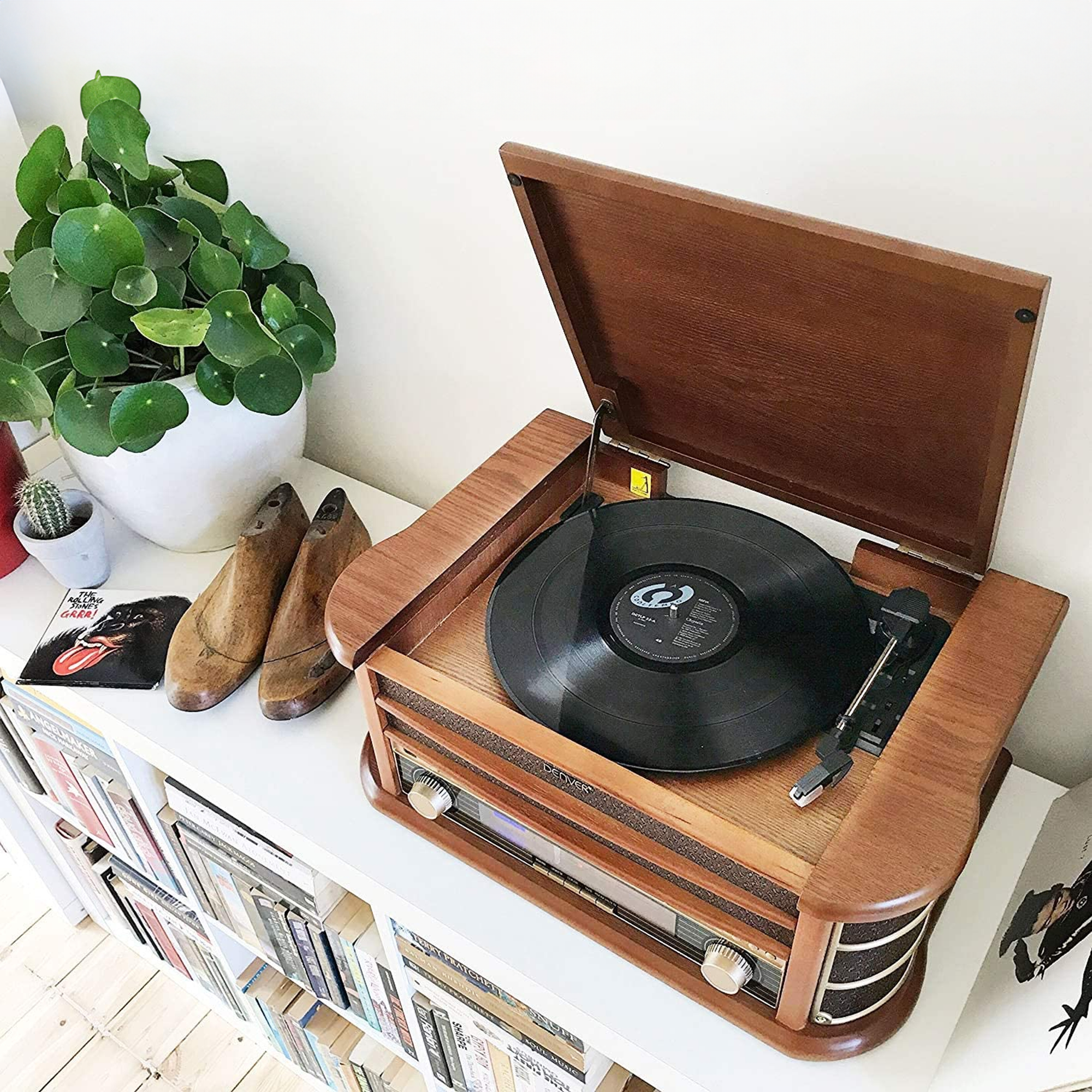 Een vintage platenspeler met zwarte vinylplaat op een plank met boeken en planten.