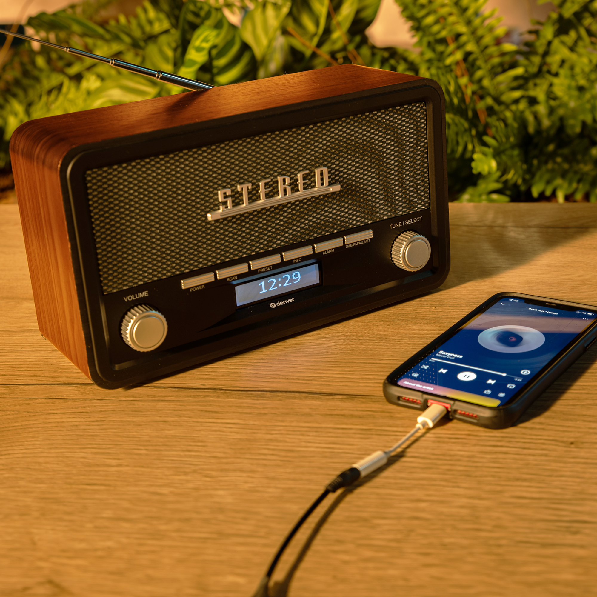 Radio retro z podłączonym telefonem. Ekran telefonu wyświetla elementy sterowania muzyką.