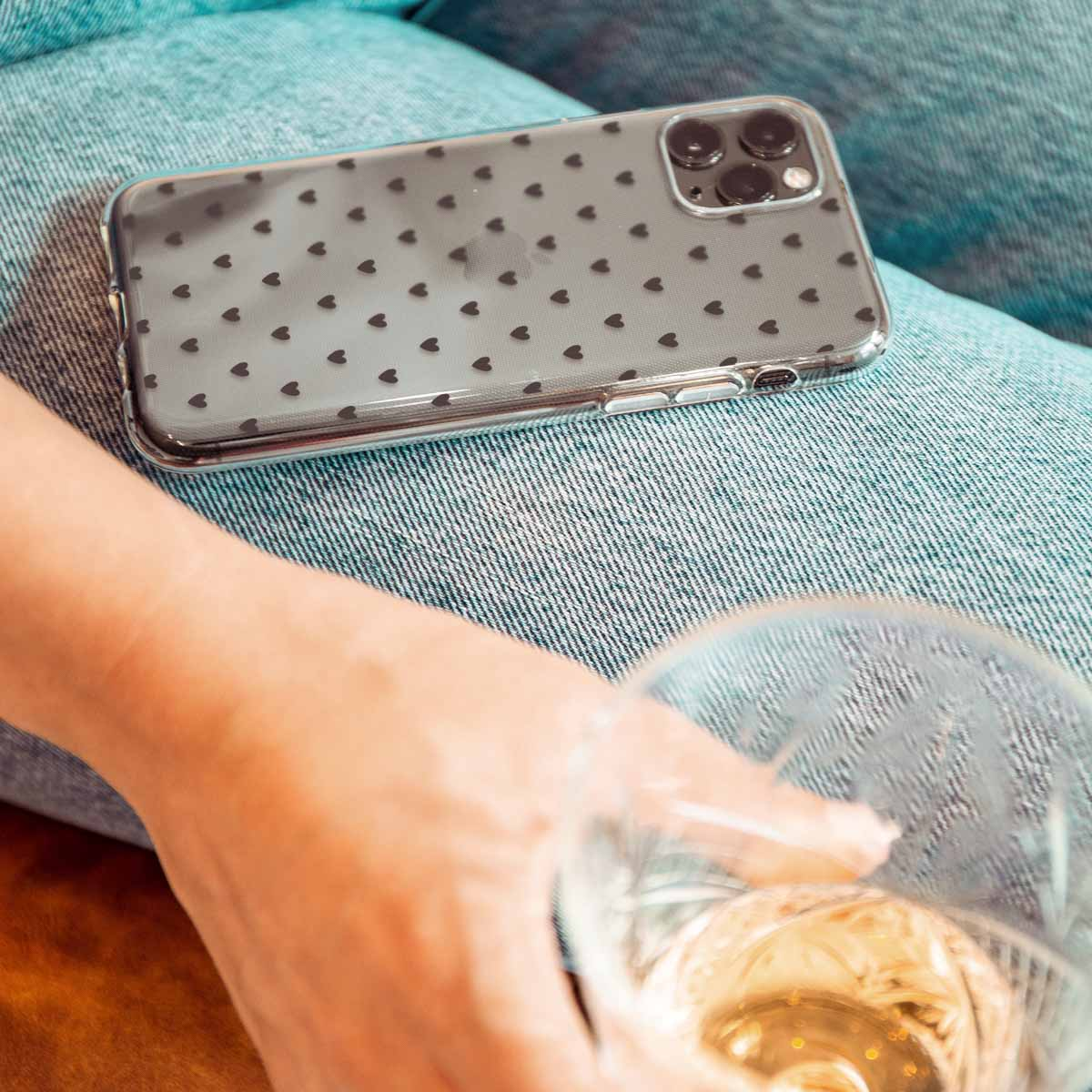 Een transparante telefoonhoes met hartjes, op een blauwe spijkerbroek. Een glas wijn is in de buurt.