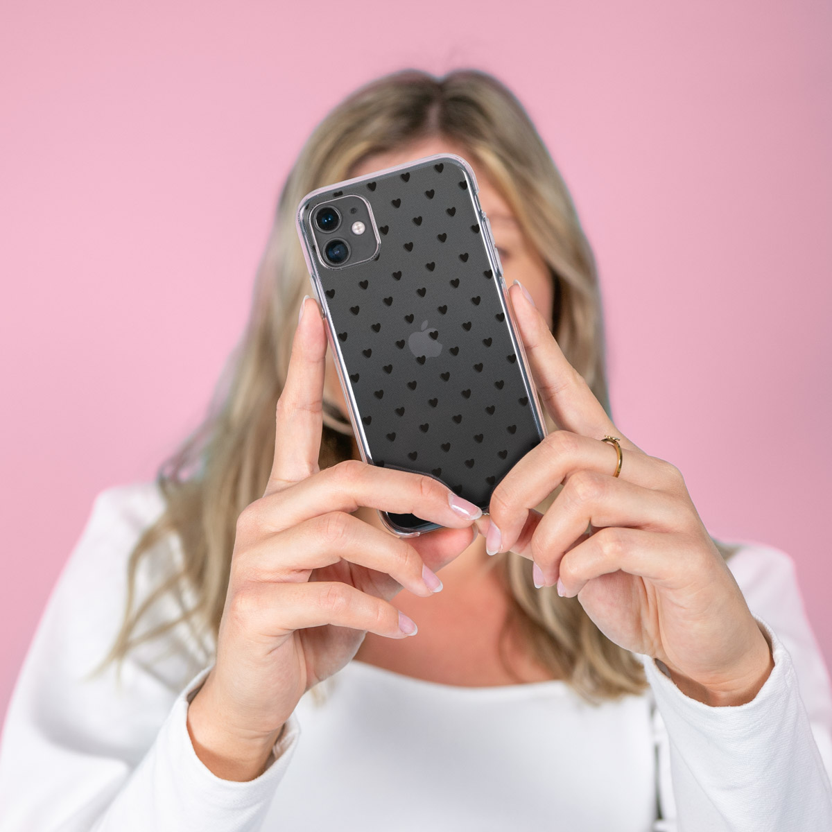 Una donna che tiene una custodia per telefono con cuori neri su sfondo rosa. Il telefono è dentro.