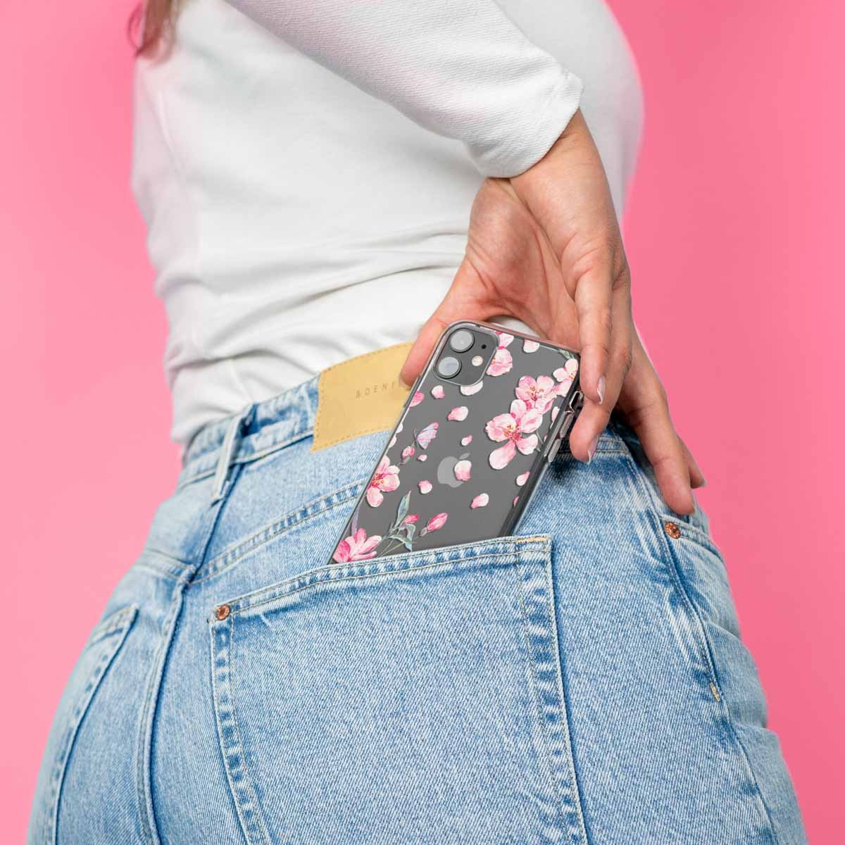 Vrouwenhand in een jeanszak, met een telefoon met een bloemenhoesje. Roze achtergrond.