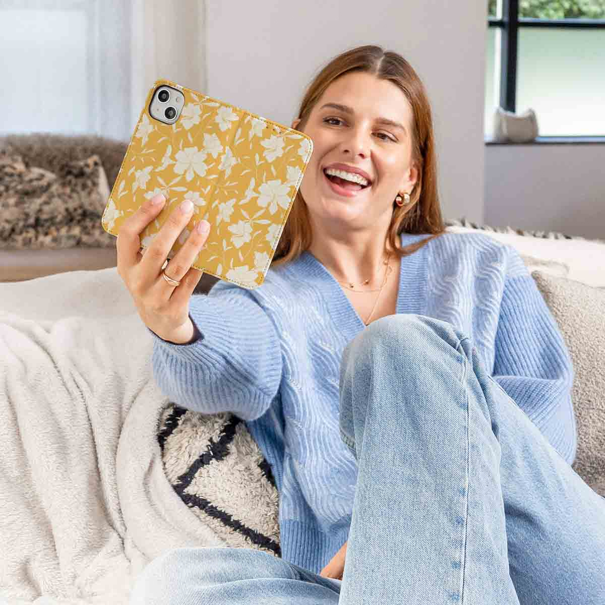 Vrouw met gele bloemen telefoonhoes. Glimlachend, draagt blauwe trui en jeans.