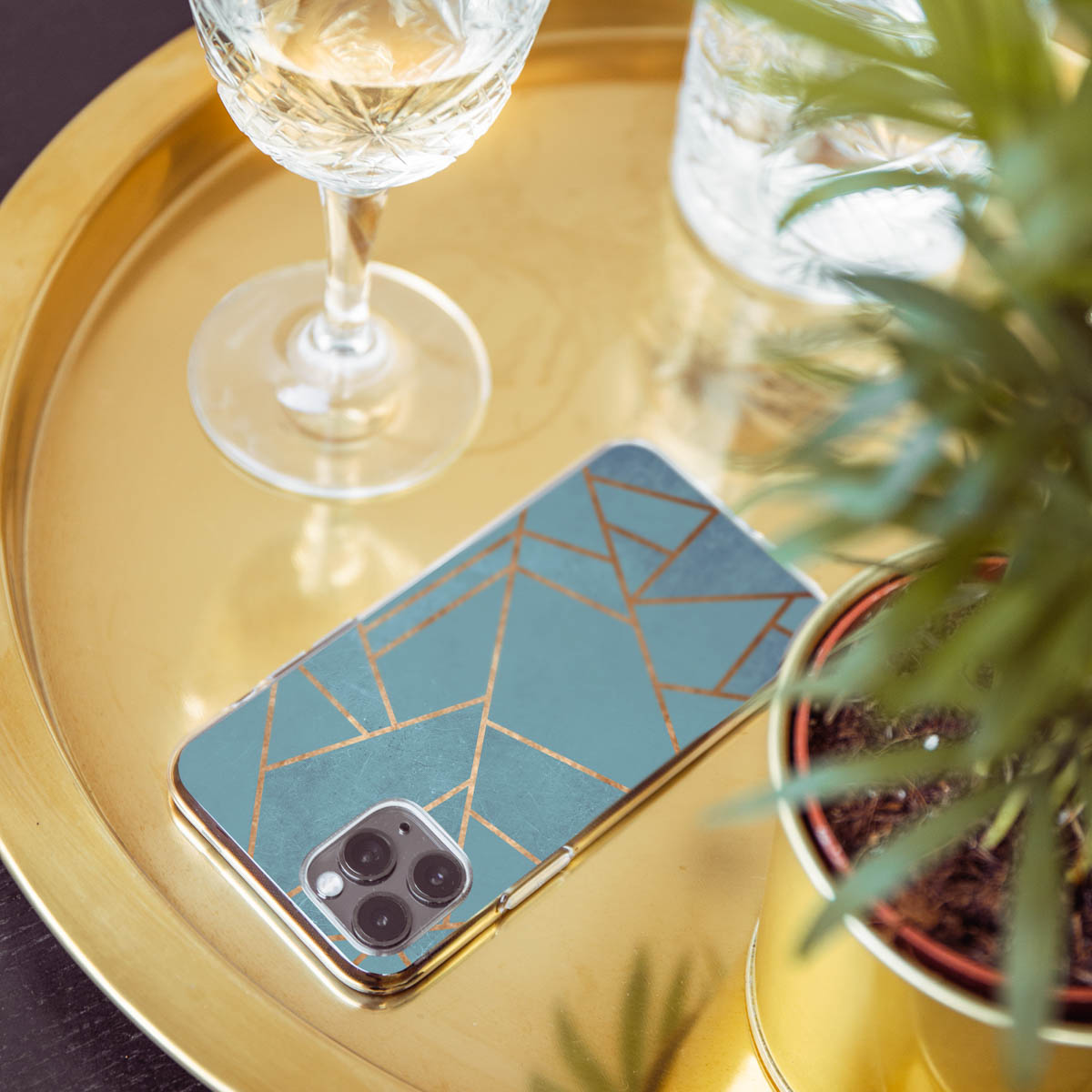 Telefon mit blau-goldenem Design auf goldener Platte mit Glas und Pflanze.