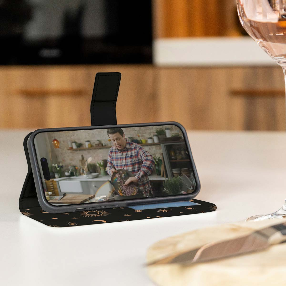 Telefoon in een hoesje met een video, een glas wijn en een houten plank op een tafel.