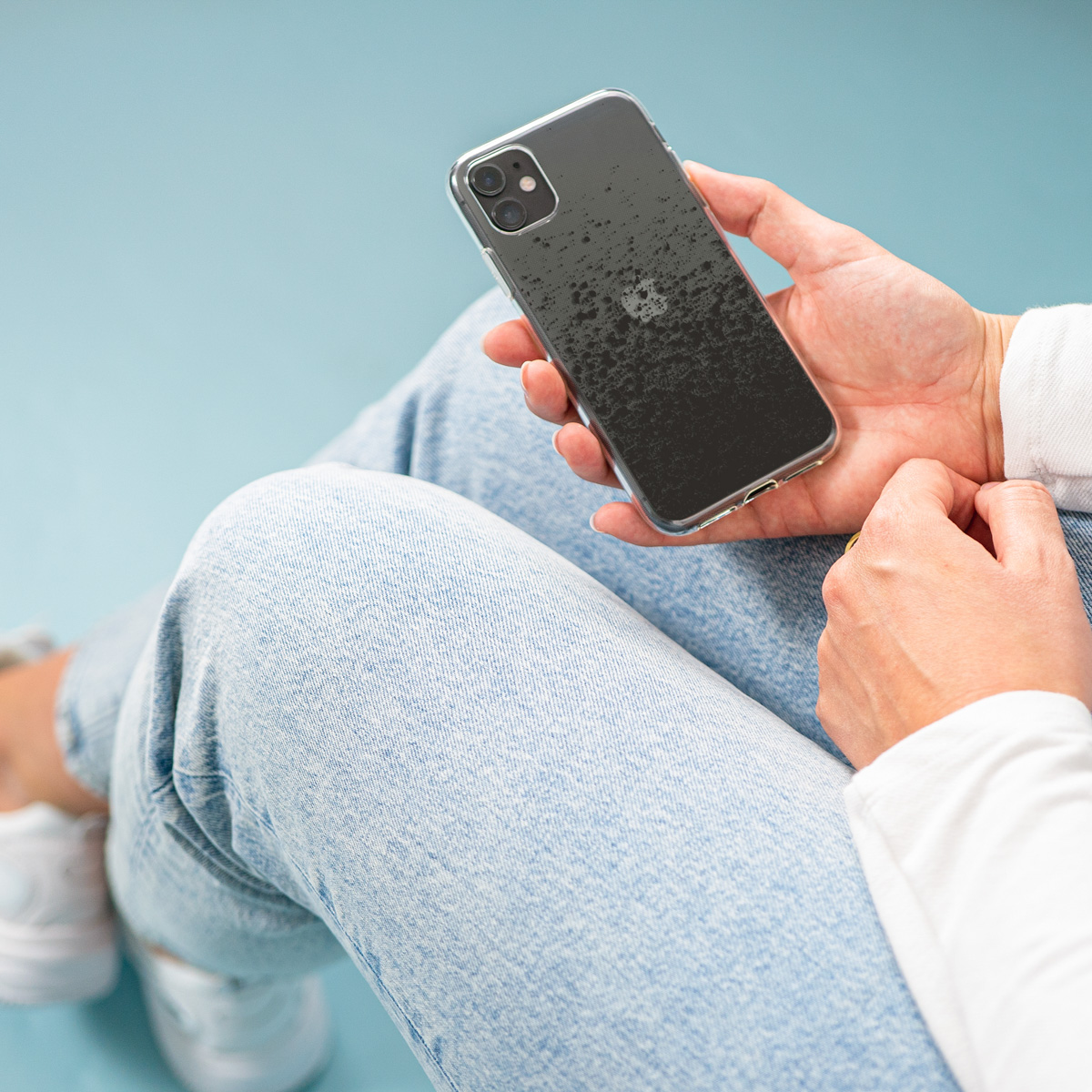 Persoon zittend met telefoon, toont zwart spatterdesign in doorzichtige hoes.