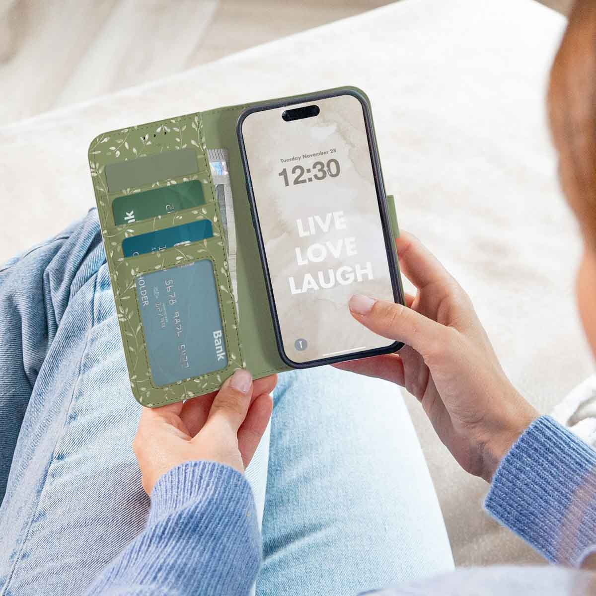Een persoon die een telefoonhoesje met een bloemenontwerp vasthoudt, met het scherm van de telefoon met de tekst 'LIVE LOVE LAUGH'.