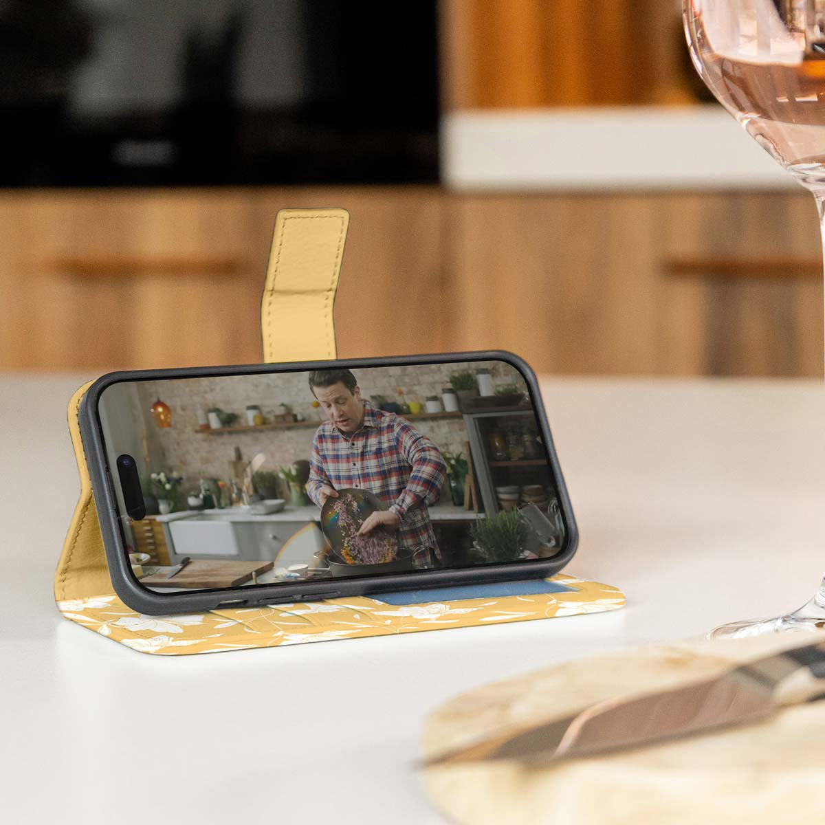 Un téléphone dans un étui jaune est sur une table. Un homme est à l'écran.