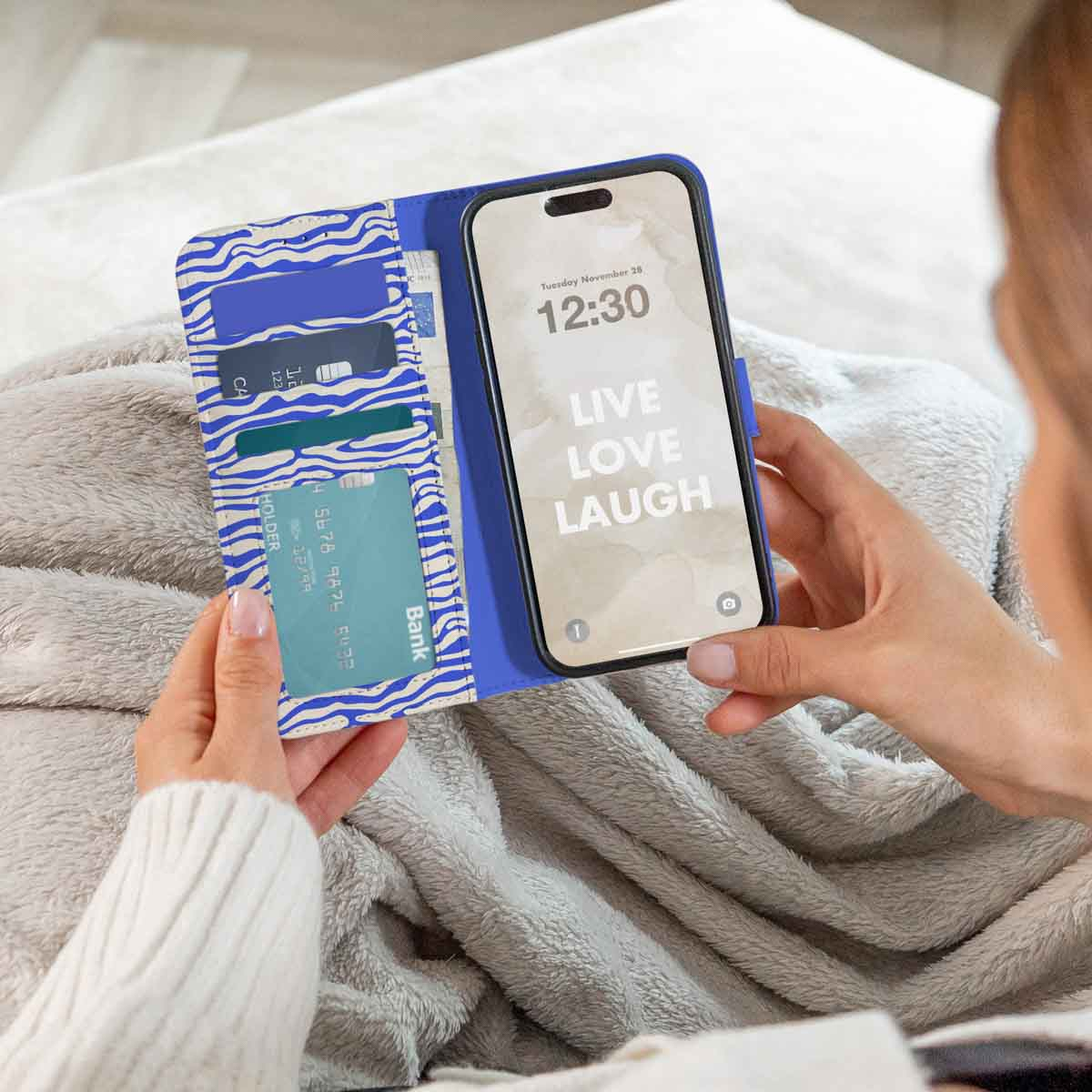 Persoon die een telefoonhoes vasthoudt met een blauwzwarte zebraprint. Het telefoonscherm toont tekst: Live Love Laugh.