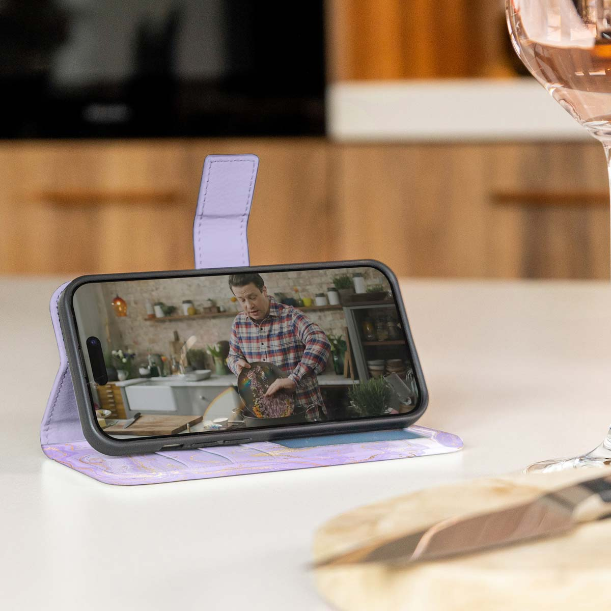 Een telefoon in een hoesje toont een video van een chef-kok. Een wijnglas in de scène.