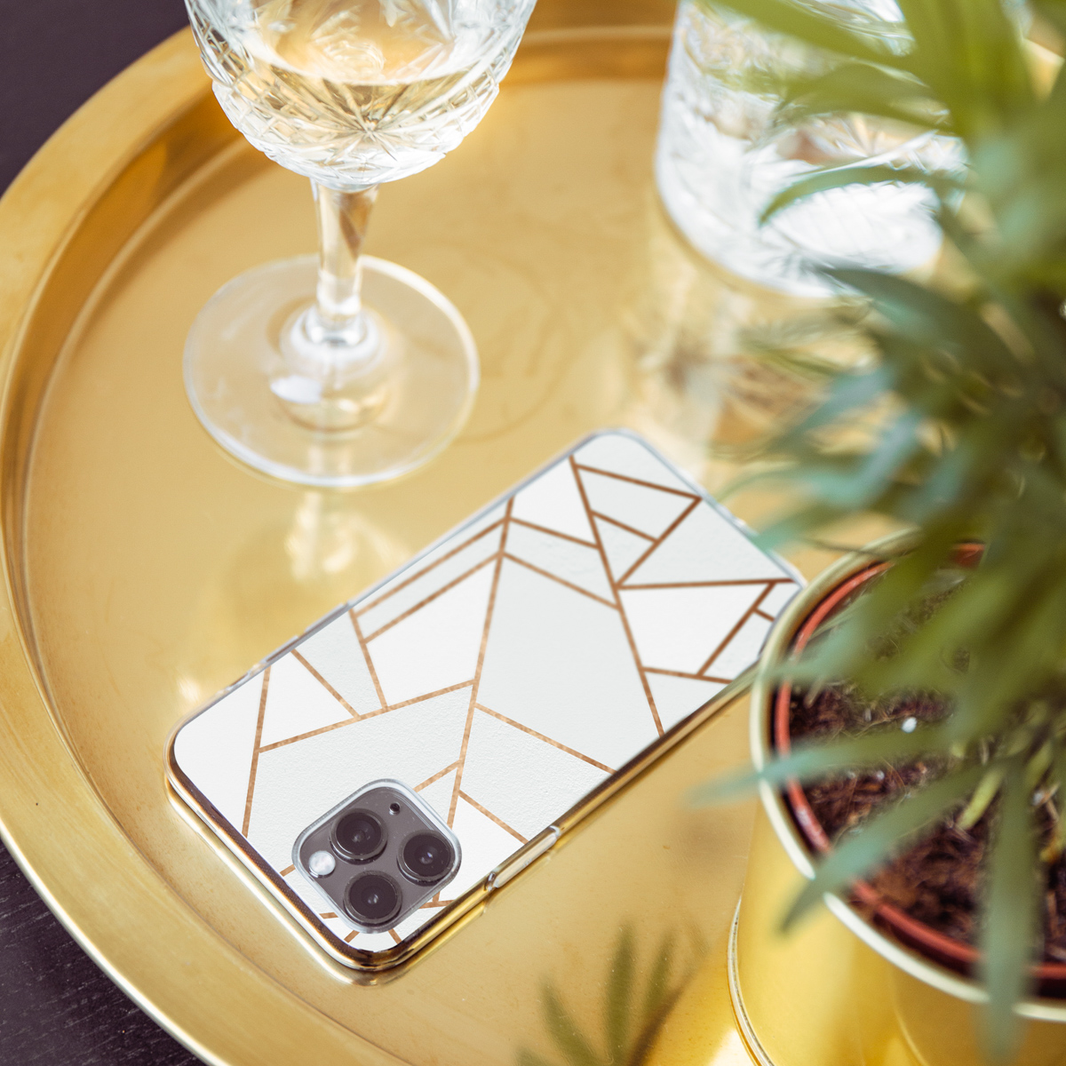 Coque de téléphone et verre sur un plateau doré. Une coque de téléphone avec un design géométrique est sur un plateau doré.