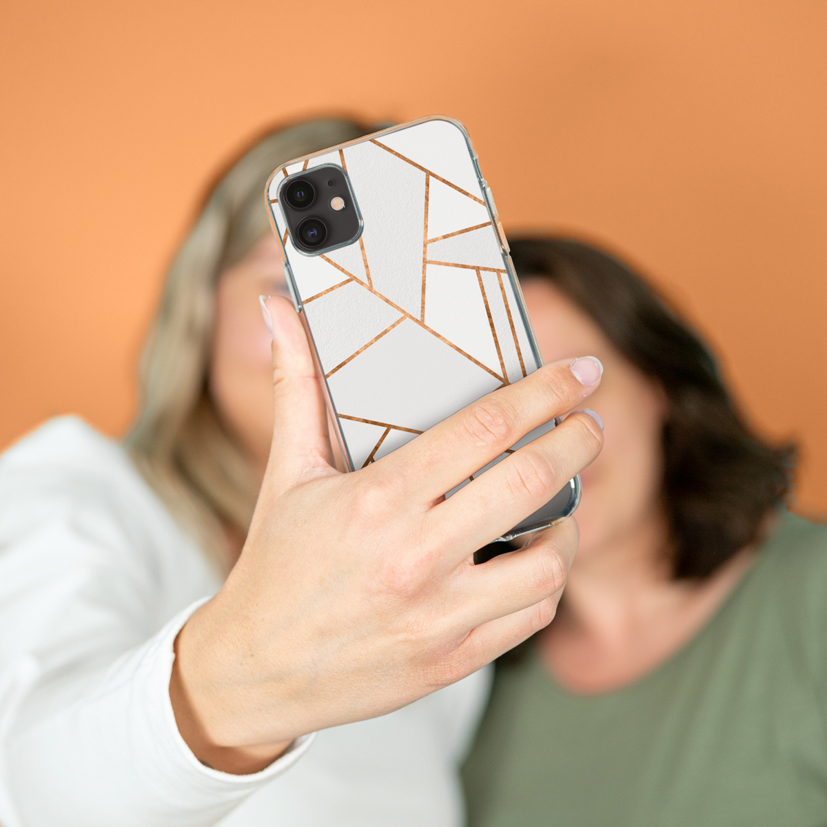 Deux femmes prennent un selfie avec des coques de téléphone. Elles tiennent des téléphones avec des motifs géométriques.