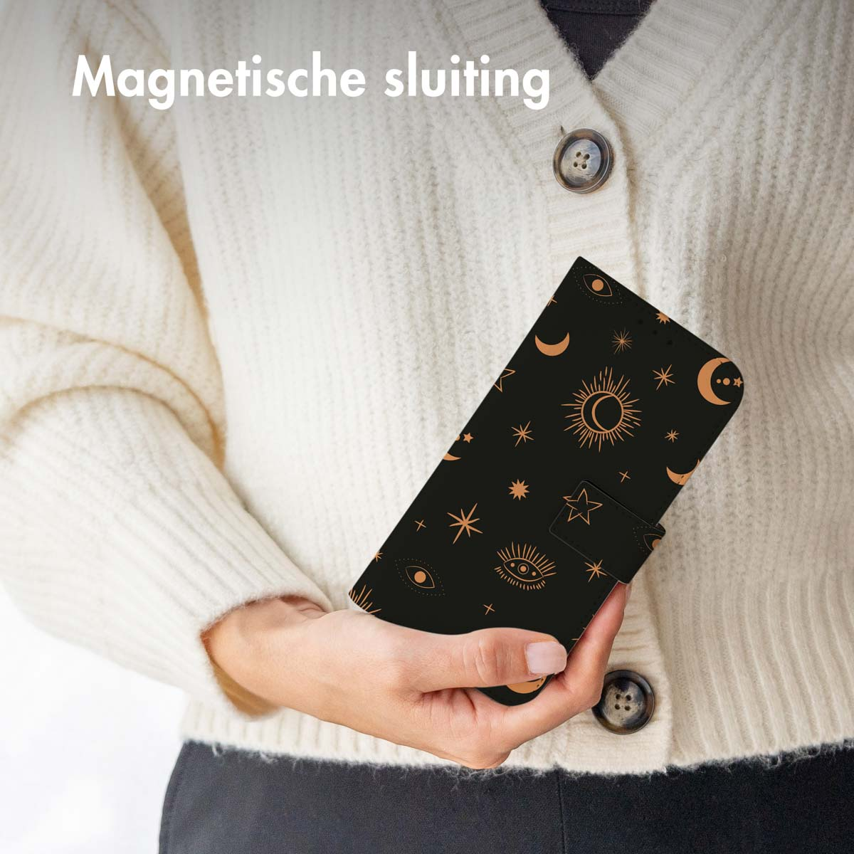 Vrouw houdt zwarte telefoonhoes met gouden hemelse ontwerpen vast, draagt een witte trui.