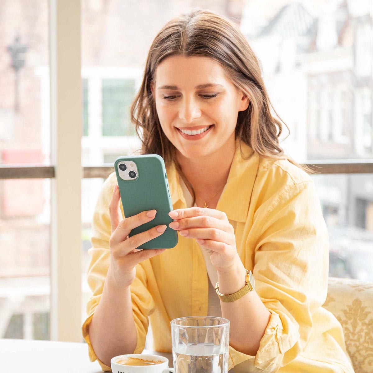 Vrouw met een groene telefoon met hoesje. Koffie en water op tafel. Binnenscène.