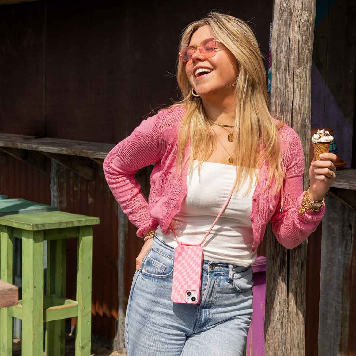 Eine Frau in rosa Outfit und Sonnenbrille, hält ein Telefon mit karierter Hülle.