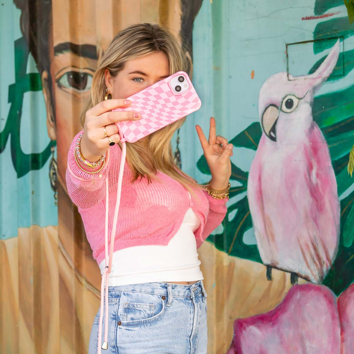 Eine Frau macht ein Selfie mit einer pink karierten Handyhülle. Im Hintergrund ist eine Wandmalerei.