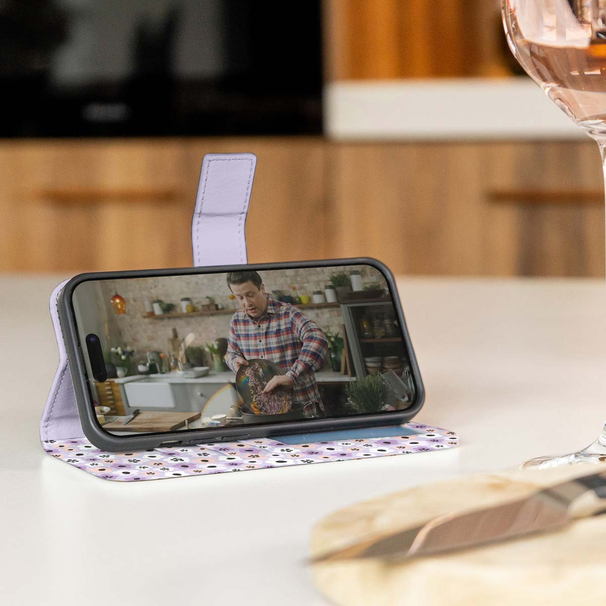 Telefoon is open, toont een video van een persoon die kookt. De hoes heeft een bloemenpatroon.