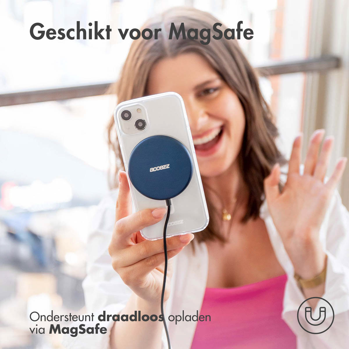 Vrouw houdt telefoon vast met blauwe MagSafe-oplader. Ze glimlacht. Wit overhemd, roze top.