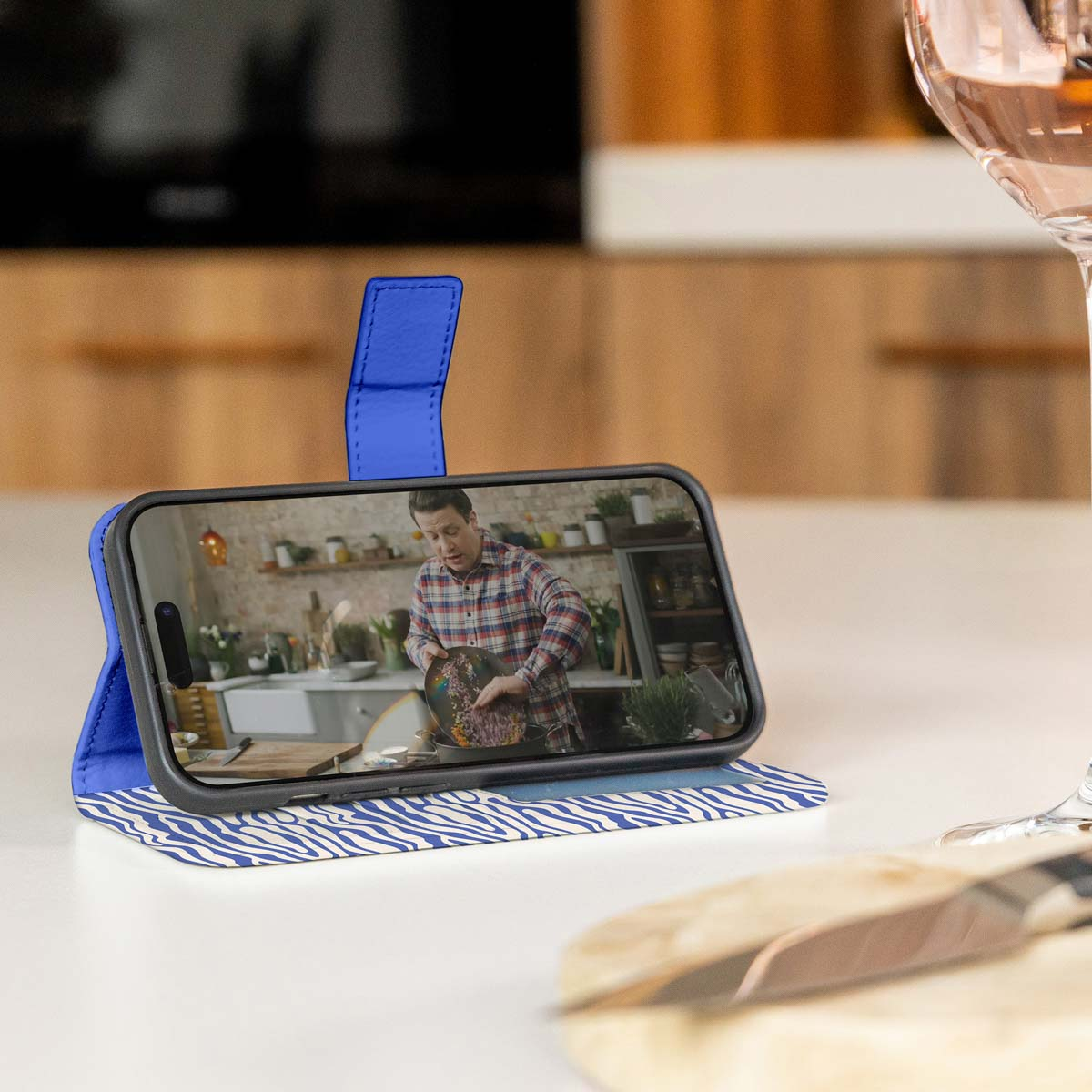 Telefoonhoes prop, met een video van een kok. Een glas wijn staat op de achtergrond.