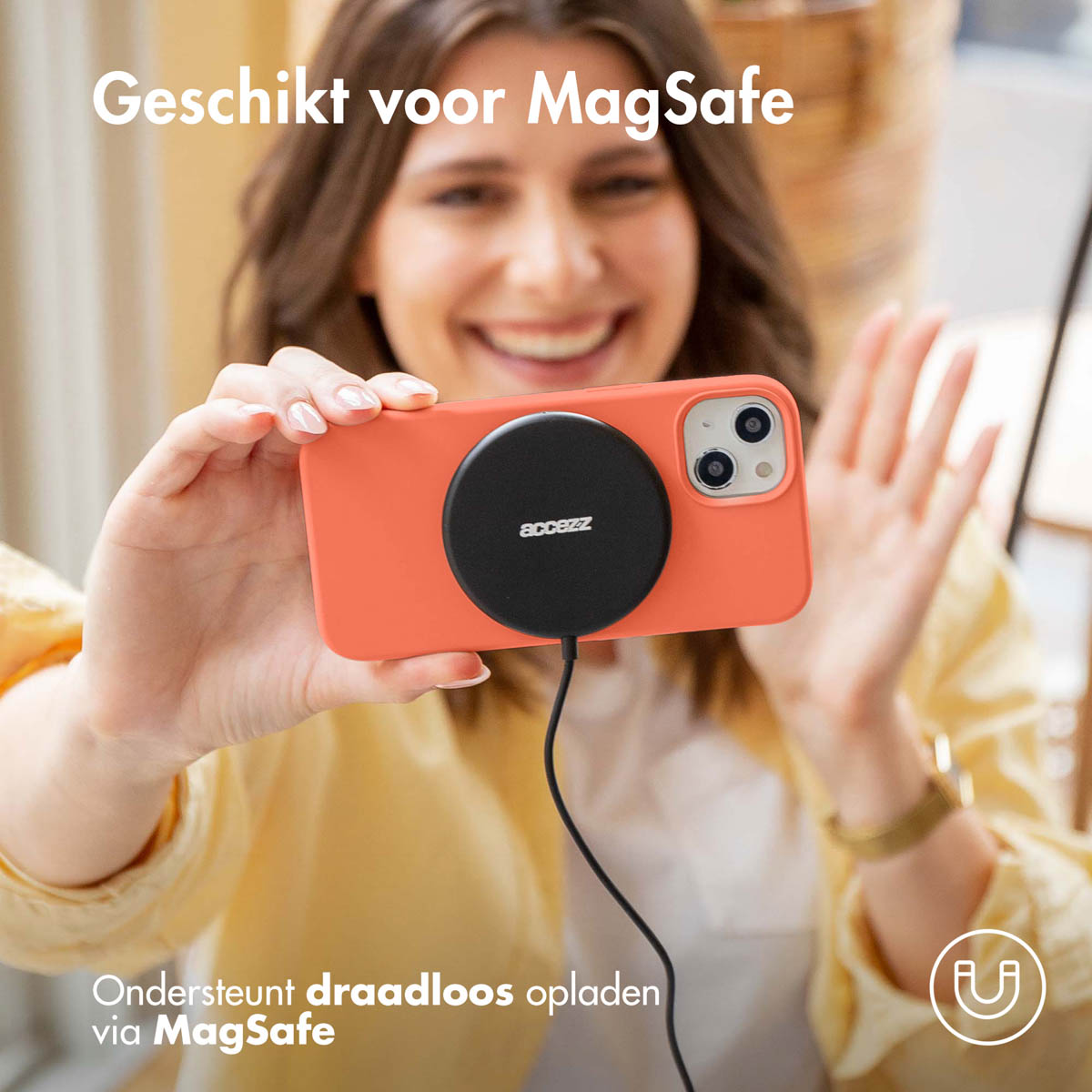 Vrouw houdt een oranje telefoon vast met een zwarte MagSafe-oplader. Tekst: Geschikt voor MagSafe en ondersteunt draadloos opladen.