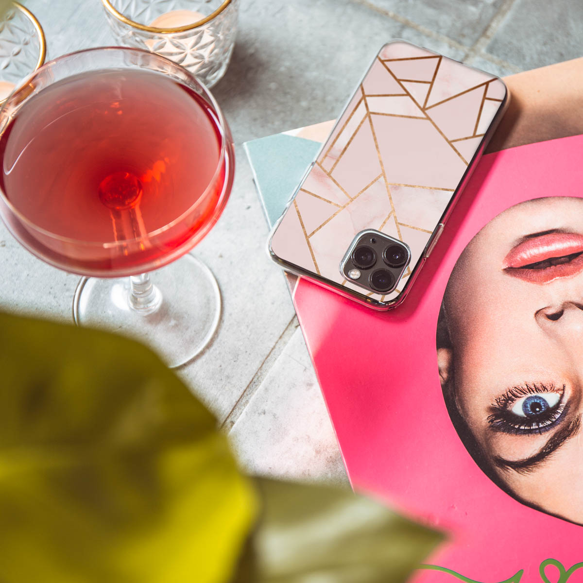 Cocktail et étui de téléphone avec design géométrique doré sur magazine et surface pierre.
