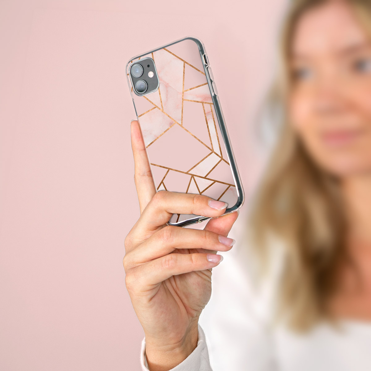 Une femme tient un téléphone avec un étui à motif marbre rose. Le fond est un dégradé rose.