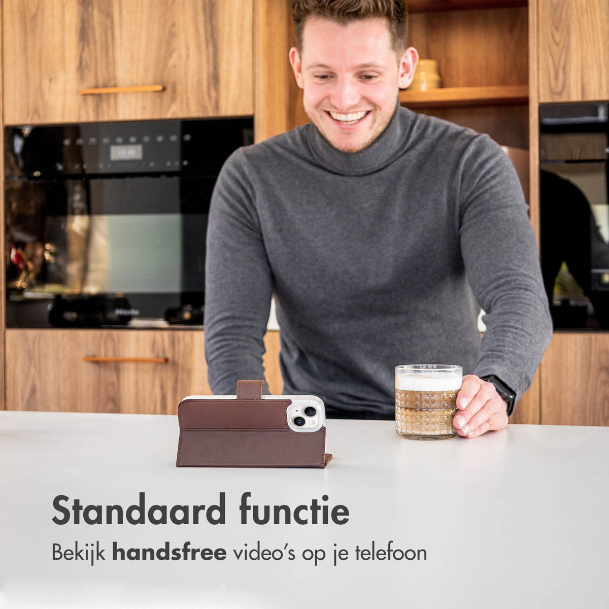 Man with a phone in a brown case, looking at the phone. A drink is on the table.