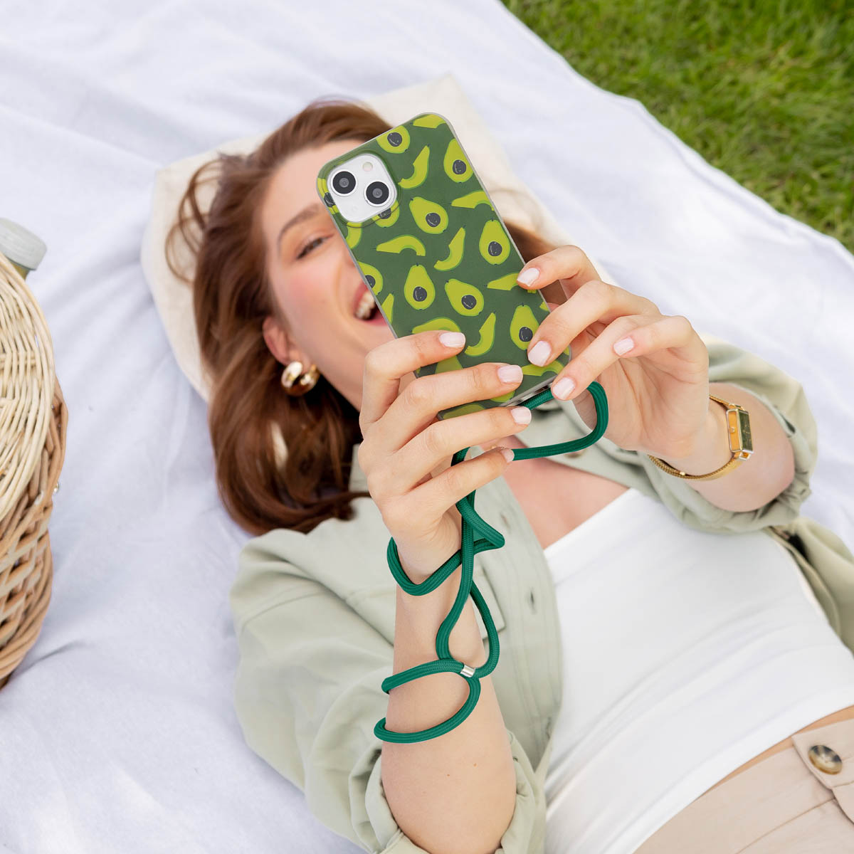 Frau auf Picknickdecke hält Telefon mit Avocado-Hülle.