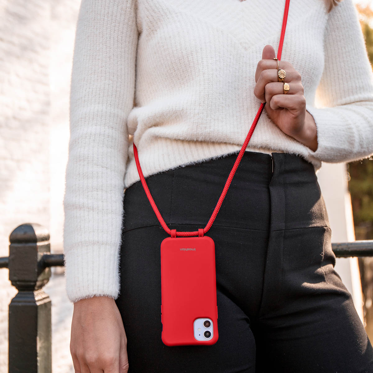Frau in schwarzer Hose und weißem Pullover hält ein rotes Telefon mit rotem Riemen.