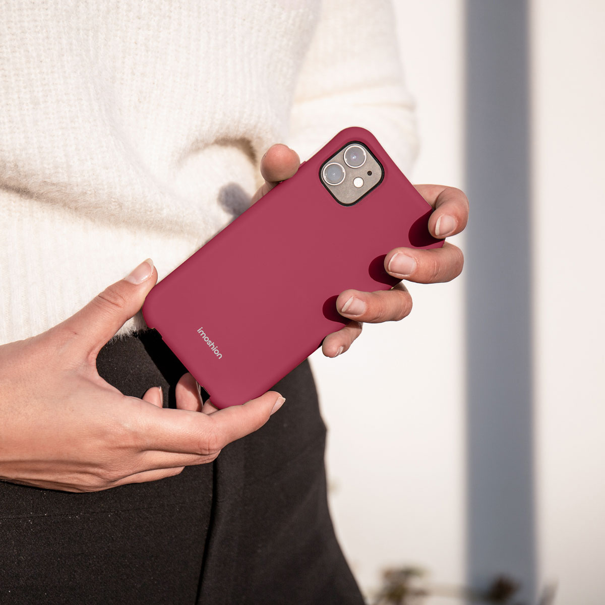 Handen van een persoon die een bordeauxrode telefoonhoes vasthouden. Witte achtergrond.