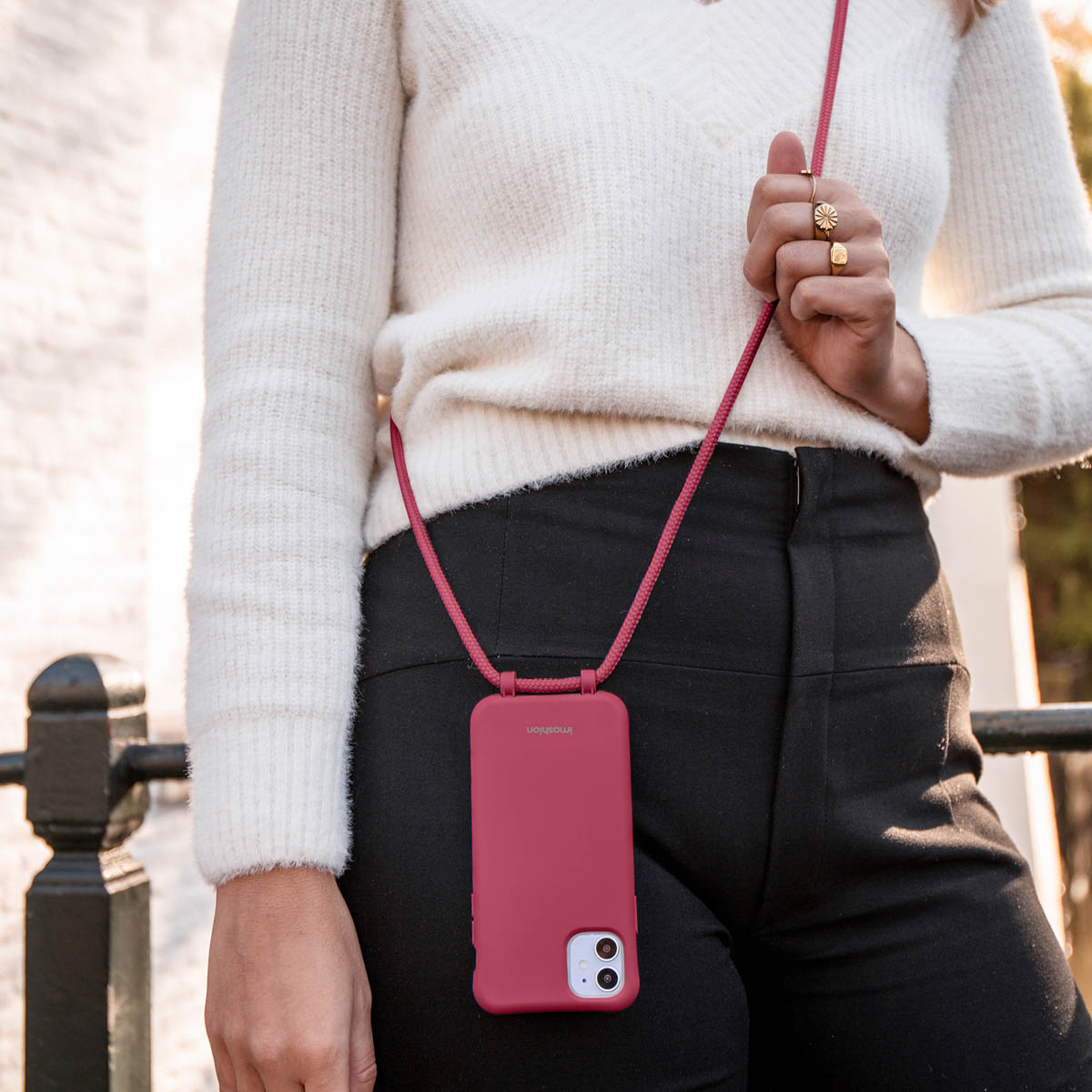 Vrouw met witte trui, rood telefoonhoesje en band.