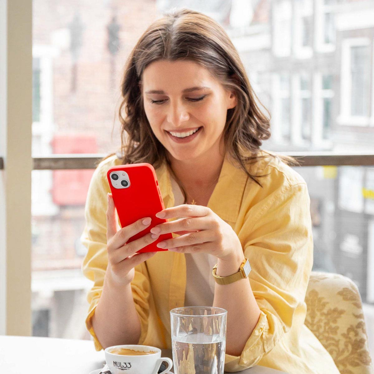 Eine Frau lächelt, während sie ein rotes Telefon benutzt. Sie sitzt an einem Tisch mit einem Getränk und Kaffee.